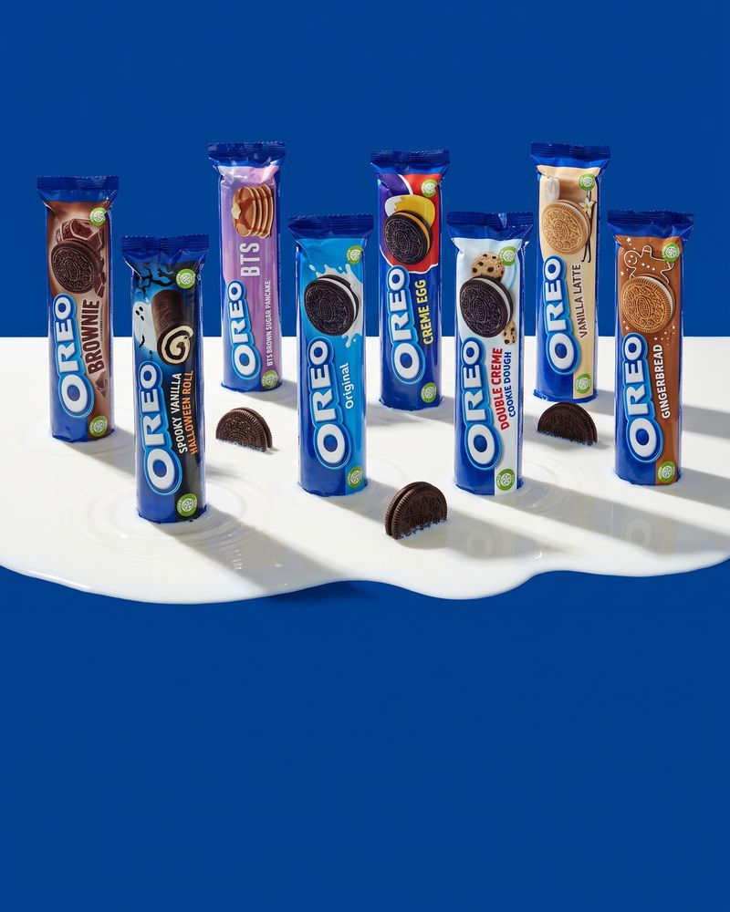 Eight Oreo rolls standing in a shallow pool of milk on deep blue — Brownie, Spooky Vanilla Halloween, BTS, Original, Creme Egg, Double Creme Cookie Dough, Vanilla Latte and Gingerbread.